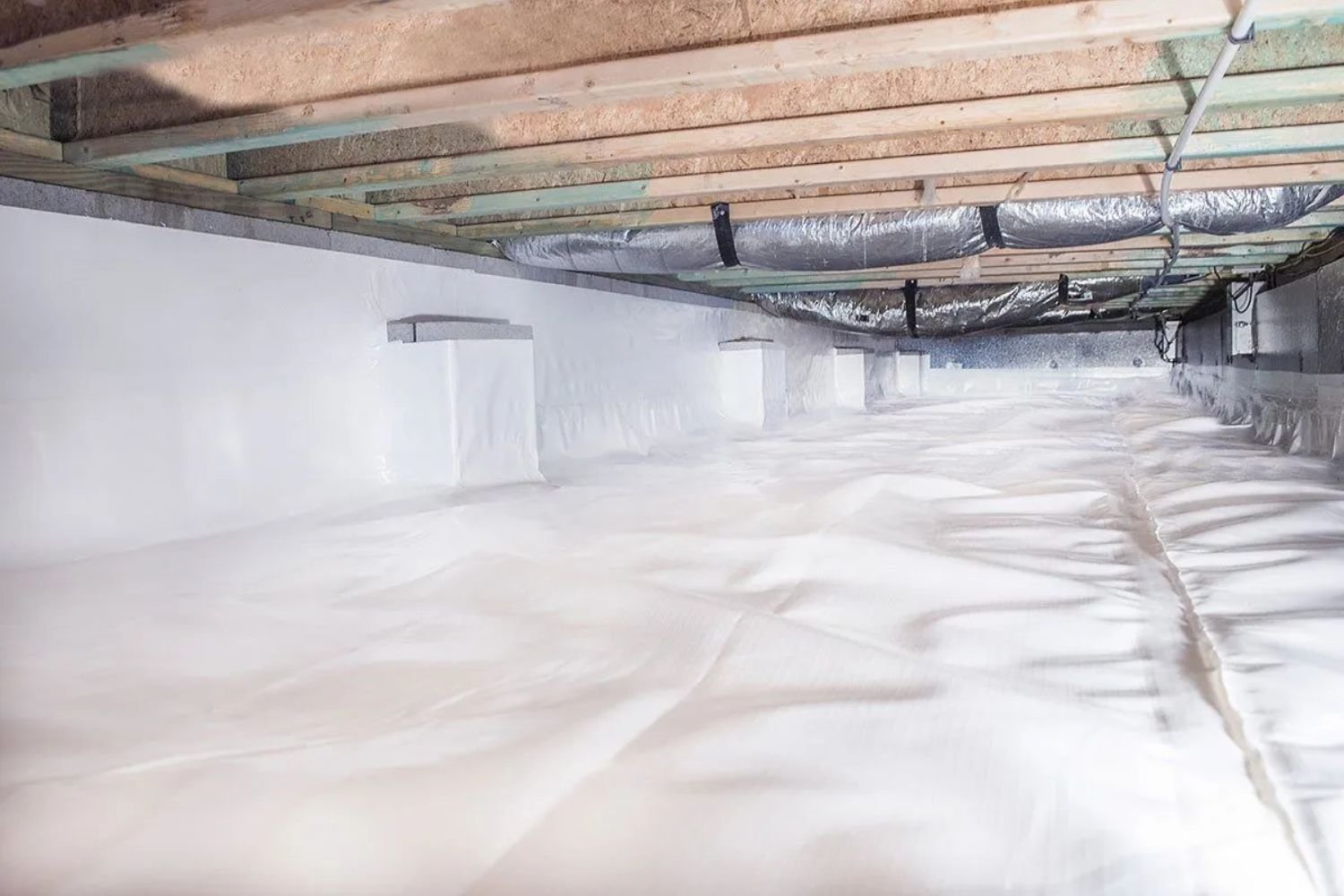 An unfinished basement showing insulation material on the walls and a white sheet laid out on the ground.