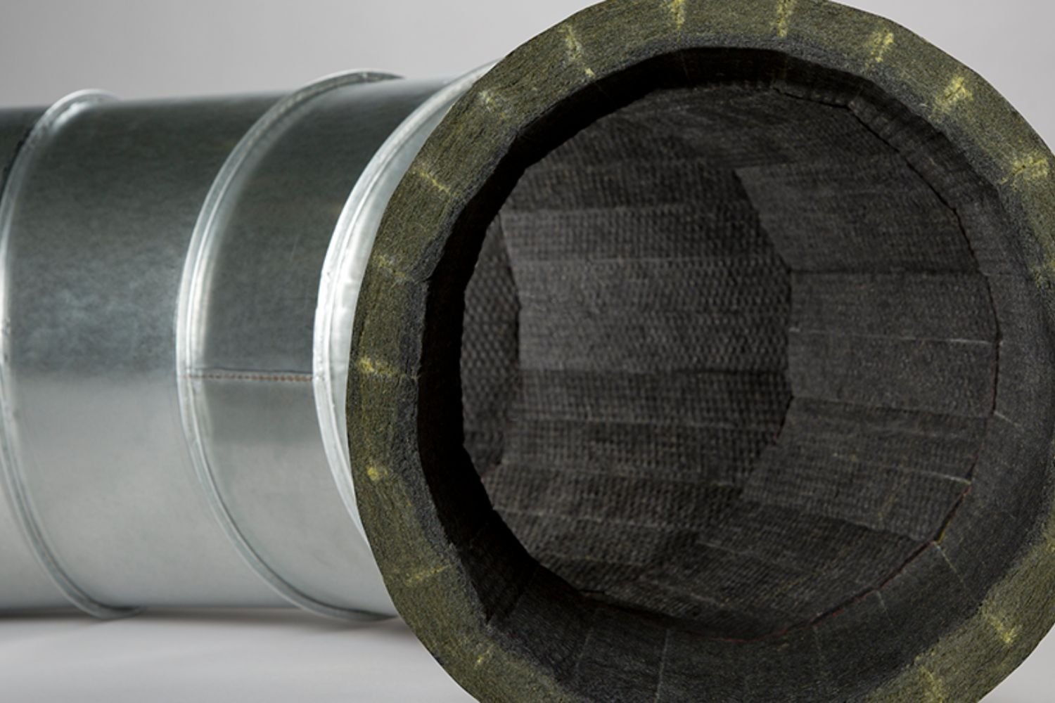 A large metal pipe covered with a black protective casing, positioned horizontally against a neutral background.